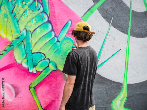 A young graffiti artist drawing street art in green and pink tones.