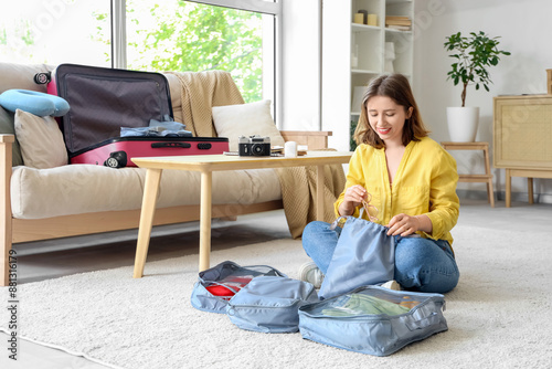 Young woman putting sunglasses into organizer while packing suitcase at home. Travel concept