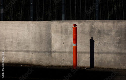 Red safety bollard casting a long shadow against a concrete wall