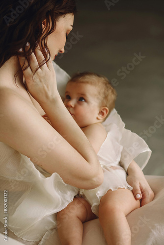 Importance Of breastfeeding concept. Beautiful mother feeding her baby girl with breast milk, sitting on sofa indoor