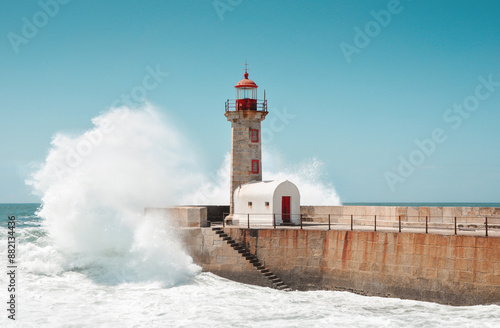 Wave crashing into lighthouse on the stone mole. The Felgueiras Lighthouse at Douro river mouth in Foz do Douro near Porto. Blue sky and Atlantic Ocean in the background.