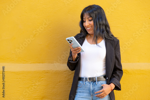 latin woman texting with her cell phone on a yellow background in la paz bolivia - communication concept