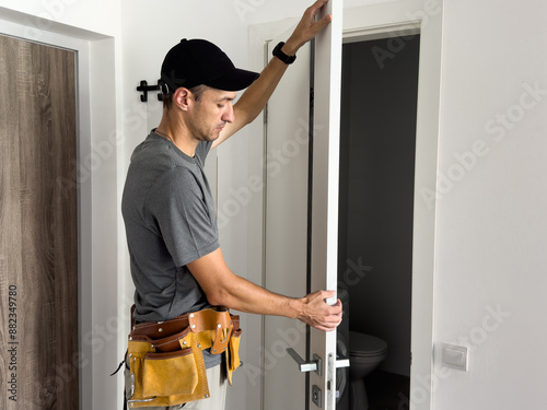 As part of process of installing interior doors in new house, a trim worker uses hammer to strike the door jambs