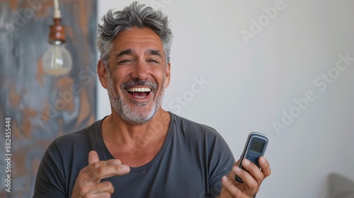 A smiling man candidly holding a phone, capturing a relaxed and happy moment. Set against a neutral background, this image radiates warmth, friendliness, and contentment.