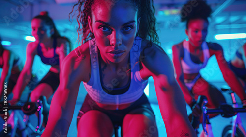 Group of athletes are participating in a cycling class in a modern gym with neon lights. The woman in front is leading the class