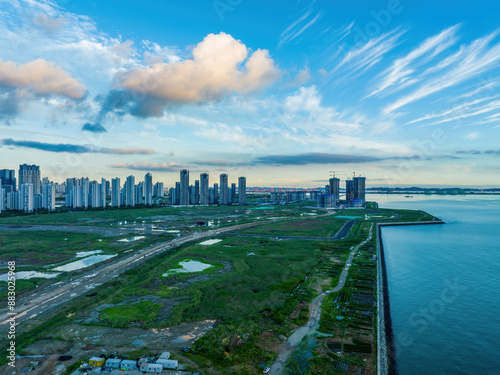 Songdo-dong, Yeonsu-gu, Incheon, South Korea - July 8, 2023: High angle view of road and wetland on reclaimed land against construction site and apartments near the sea 