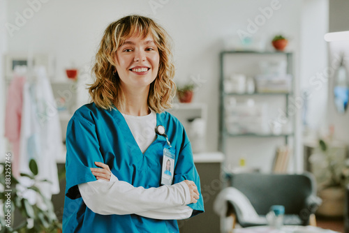 Golden haired Caucasian nurse smiling widely and crossing her arms while sitting for portrait in on call room