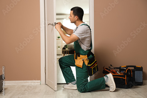 Male worker with screwdriver repairing door at home