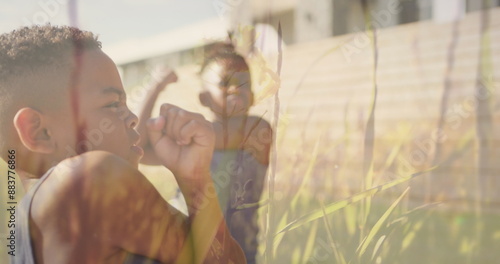 Image of grasses over happy diverse schoolboys stretching in outdoor yoga class