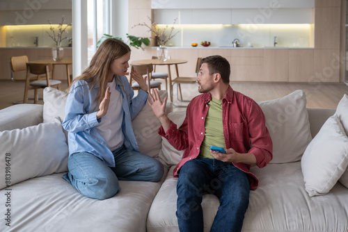 Secretive, insincere husband brushing off irritated woman reproaches for infidelity. Angry disgruntled girl accusing guy for cheating. Spouses fighting arguing squabbling on sofa in living room.