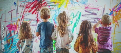 Five children stand facing a wall covered in colorful, abstract drawings. They appear to be engrossed in their artwork, each adding their own creativity.