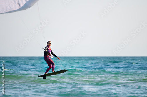 Young Caucasian woman athlete ride on a hydrofoil board with a kite in the open ocean. Hydrofoil is a new direction in kitesurfing