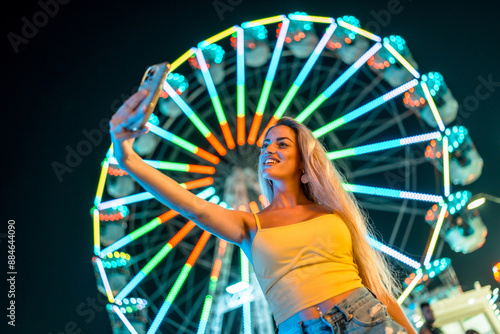 Woman taking a selfie next to ferris wheel at night