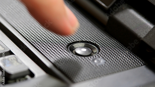 Man's finger about to press the laptop computer power button, hovering over the power on key about to boot, start or restart the device, one person, object detail closeup, side view. Turning on or off