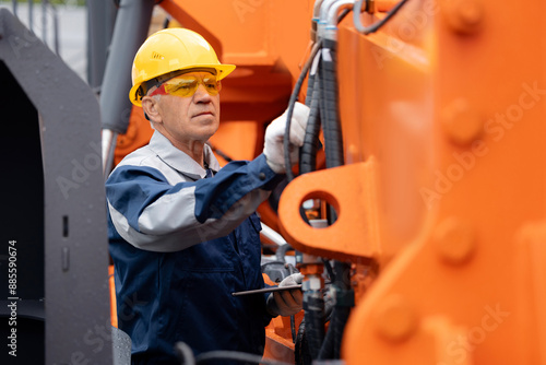 Mechanic repairing hydraulic hose in drilling machine, exploration drilling. Adult man in hard hat industrial worker.