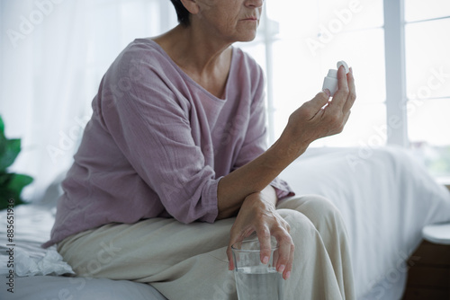 Partial shot of mature woman holding water and antidepressants on bed