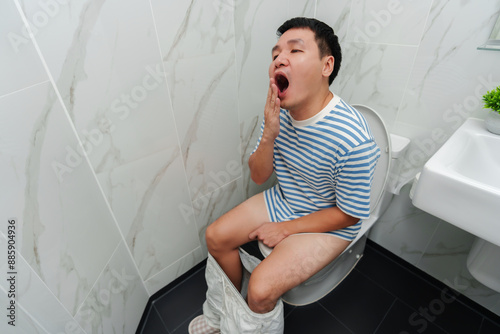 man sleepy and yawning while sitting on toilet bowl in bathroom