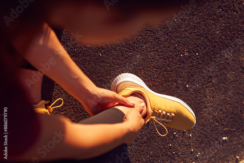 Young woman with ankle and leg pain during jogging and exercise in urban park.