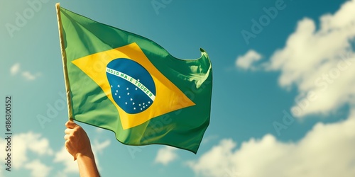 Hand holding Brazil national flag on blue sky. Happy Independence Day, Labor Day, Proclamation of the Republic. Background with copy space for greeting card, banner, poster