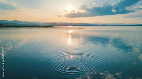 Tranquil lake at sunset with distant mountains and stone skipping waves, creating a peaceful and serene nature landscape scene.