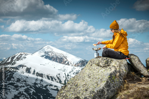 Young woman prepares food while sitting on top of a rocky mountain. Concept of escape and solitude