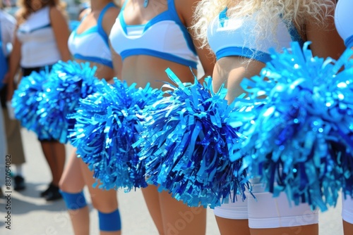 A group of cheerleaders hold blue pom poms and smile, wearing white and blue uniforms