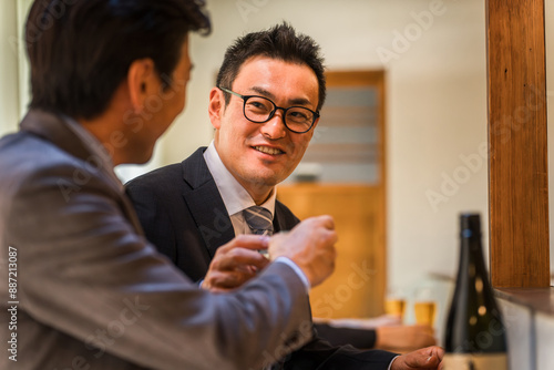 居酒屋・飲み屋のカウンターで部下と楽しくお酒を飲むビジネスマンの男性 