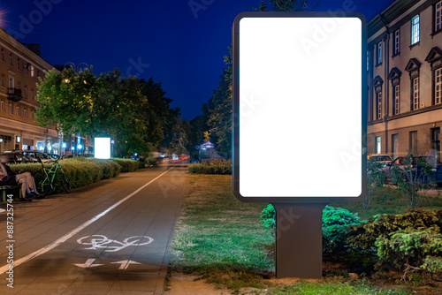 Blank White Billboard Mockup On Pedestrian Street Next To Bike Path At Night. Advertising Poster Lightbox For Commercial Branding