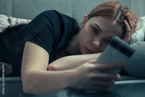 The girl is procrastinating: lying with a phone in her hands, a lazy expression on her face, a concentrated look