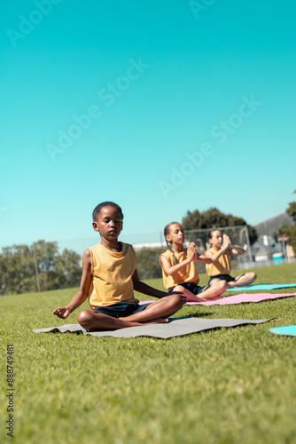 Composite of diverse schoolgirls meditating while sitting on mats over grassy field under clear sky