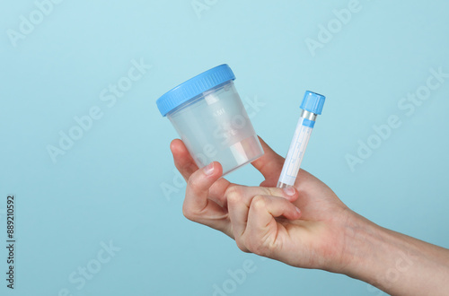 Hand holding empty blood test tube and Urine test jar on a blue background