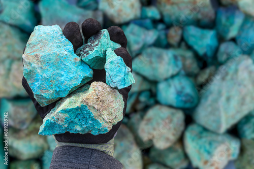 Blue green copper (Cu) oxide ore, held in hand with protective glove, against background of ore that is out of focus. Mining.