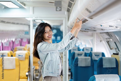 Young Woman Stowing Luggage in Overhead Compartment on Airplane with Colorful Seats