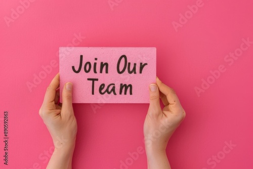 Hands Holding a 'Join Our Team' Sign Against a Pink Background