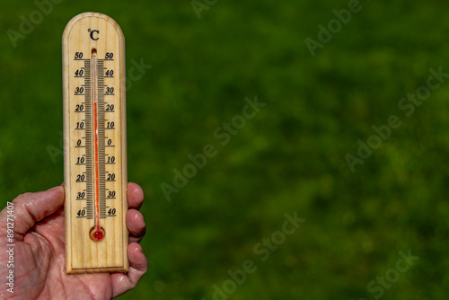 A man holds a wooden thermometer in his hand in the garden which indicates a very high temperature