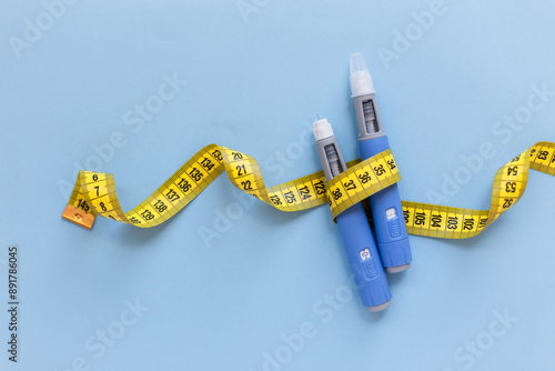 Two injectors dosing pens for subcutaneous injection of antidiabetic medication or anti-obesity medication hovering over a blue background. Yellow measuring tape around the injectors. antidiabetic