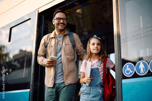 Happy father and daughter getting of bus at station.