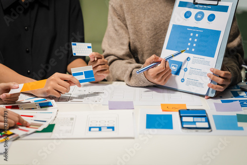 Close-up of hands working on UX/UI design at a desk. Papers with wireframes, prototypes, and mockups detail user flows, personas, and A/B testing, ensuring usability and responsive design.