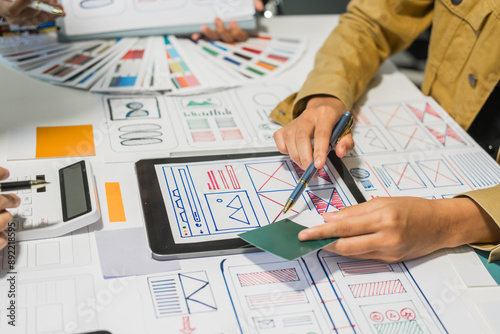 A group of people collaborates around a desk, discussing and reviewing user interface (UI) and user experience (UX) elements. usability, accessibility, and design principles for product development.