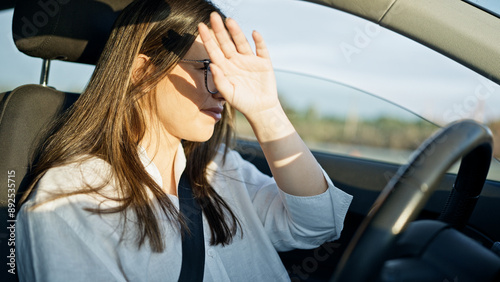 Young beautiful hispanic woman driving a car with sunlight on face on the road