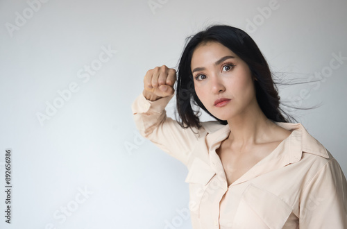 Angry upset unhappy young adult Asian woman with angry or furious expression, raising her threatening fist, ready to fight and punch right away