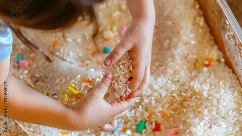 Child exploring a sensory bin filled with rice and small toys, focusing on their hands and the sensory materials 