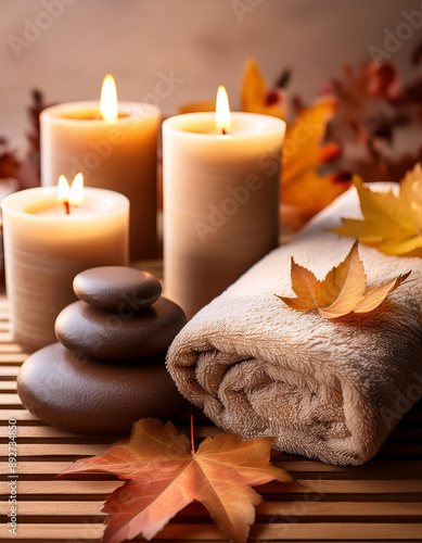 Cozy spa setting with candles, smooth stones, soft towels and autumn leaves on warm wooden surface