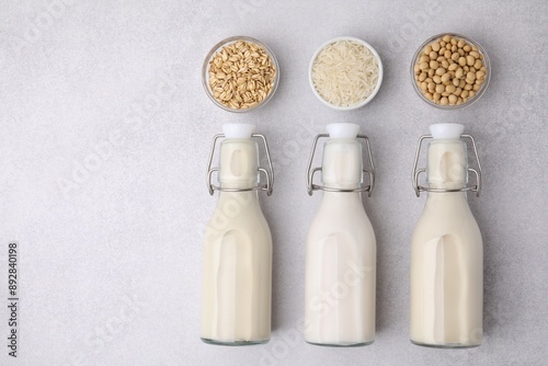 Different types of vegan milk in bottles and ingredients on light grey table, flat lay. Space for text