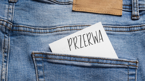 White card with a handwritten inscription "Przerwa", inserted into the pocket of blue pants jeasnow (selective focus), translation: Break