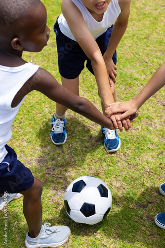 A group of young friends gathers hands over a soccer ball at school
