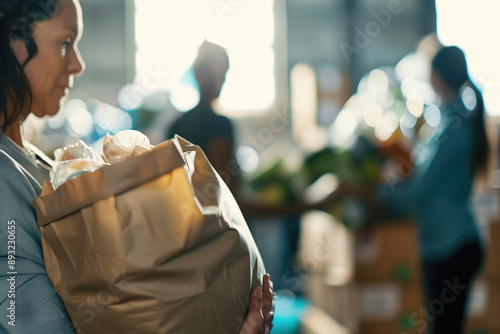 Woman holding a paper bag filled with groceries in a food donation center, volunteers in the background. Community service, charity, food bank, volunteerism, social aid, helping others.