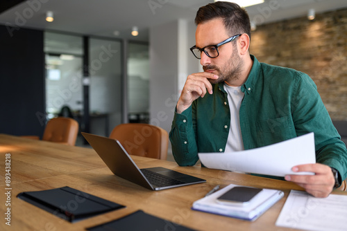 Focused young businessman auditing revenue report and planning budget while working at desk in office