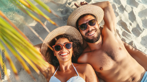 Happy couple sunbathing on a tropical beach under a palm tree