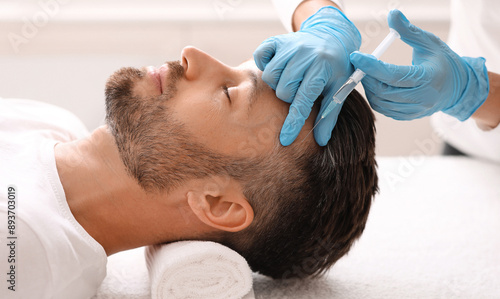 Side view of handsome middle aged man getting hair treatment at beauty salon. Man having mesotherapy session at aesthetic clinic, therapist hands in gloves making injection in scalp, closeup